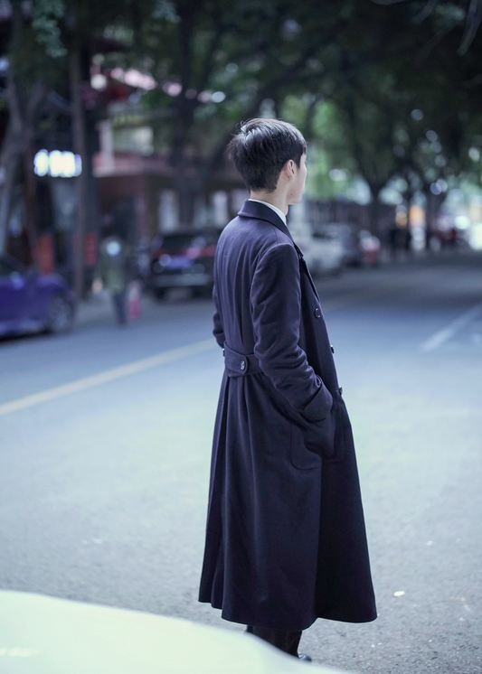 Side back view of model wearing Moonland's dark blue polo coat for men outdoors. fabric from Loro Piana cashmere, half back belt with buttons