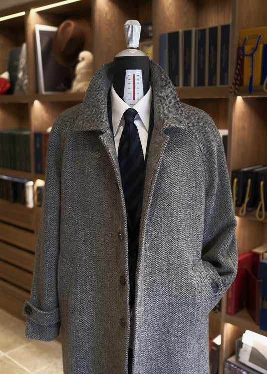 front view of Moonland's Balmacaan coat for men, made of Harris Tweed grey tone herringbone pattern. convertible collar, single breasted, raglan sleeves with tab cuff, side welt pockets