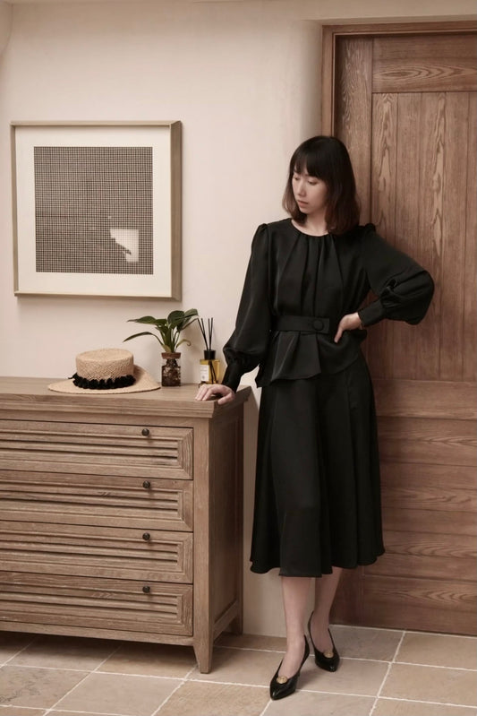 Moonland Silk Ripple Pleat Blouse, in black color, front view, gathered round neckline, long puff sleeves with volume, cuff with covered round buttons, pleated peplum with self belt at the front and a large covered button, paired with midi skirt to calf length, A-line silhouette with soft drape