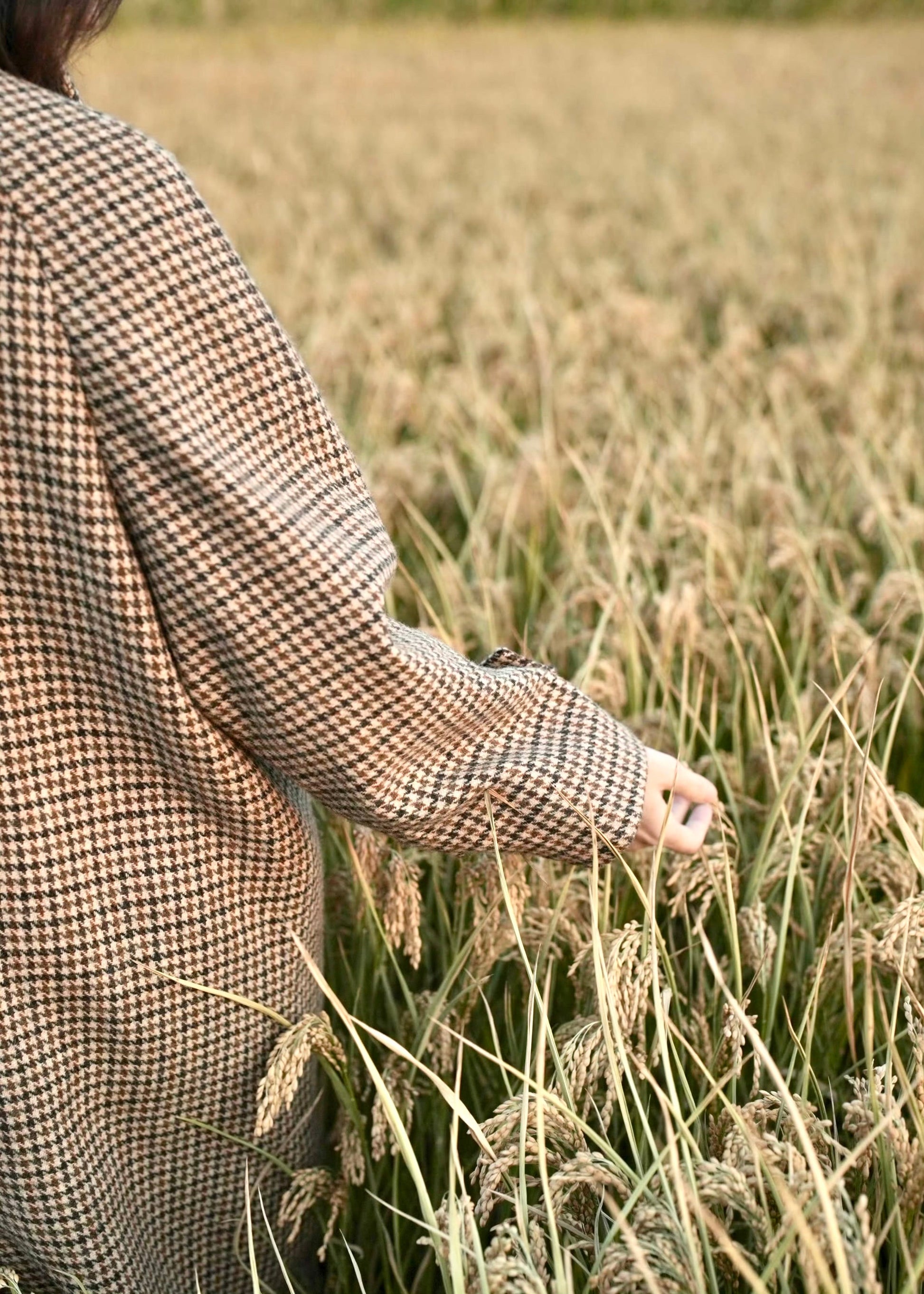 long balmaccan coat made with 100% wool with brown houndstooth or checkered pattern for women standing in front of a field at sunset