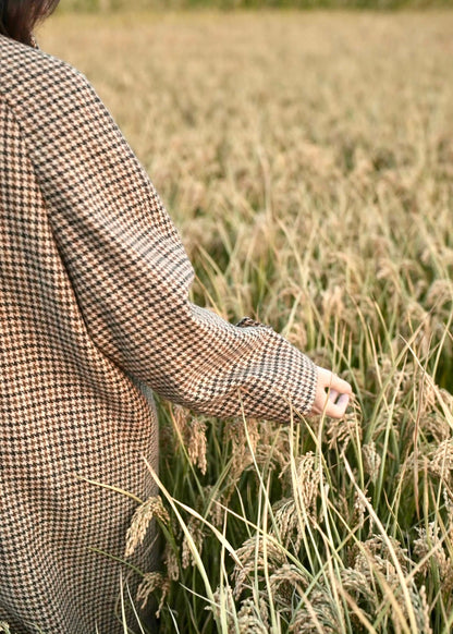 long balmaccan coat made with 100% wool with brown houndstooth or checkered pattern for women standing in front of a field at sunset