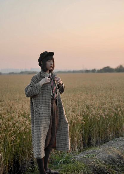 long balmaccan coat made with 100% wool with brown houndstooth or checkered pattern for women standing in front of a field at sunset