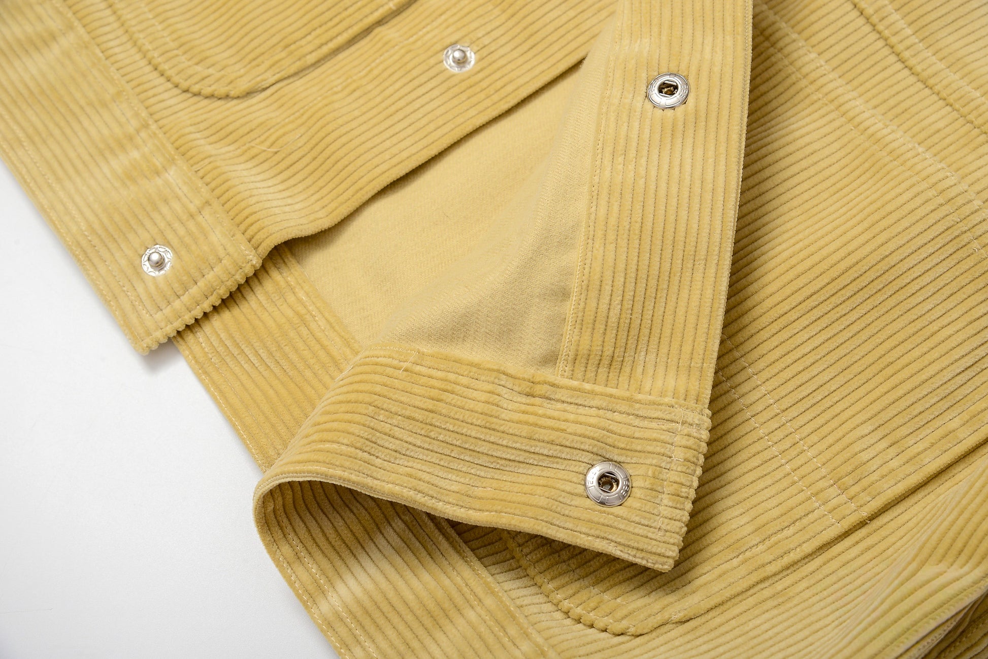 Close-up of a mustard yellow corduroy jacket with silver buttons on a light gray background #color_creamy-yellow