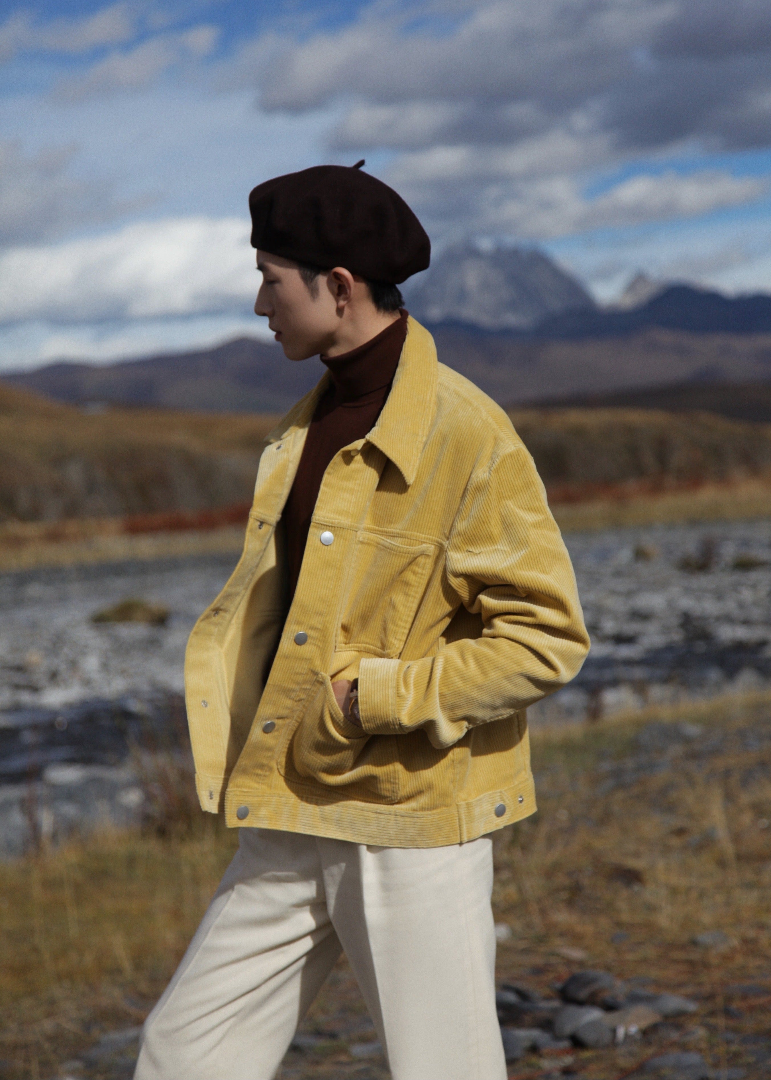  Model wearing Moonland creamy yellow corduroy workwear jacket, side profile in nature landscape, shiny silver snap button, with large patch pocket