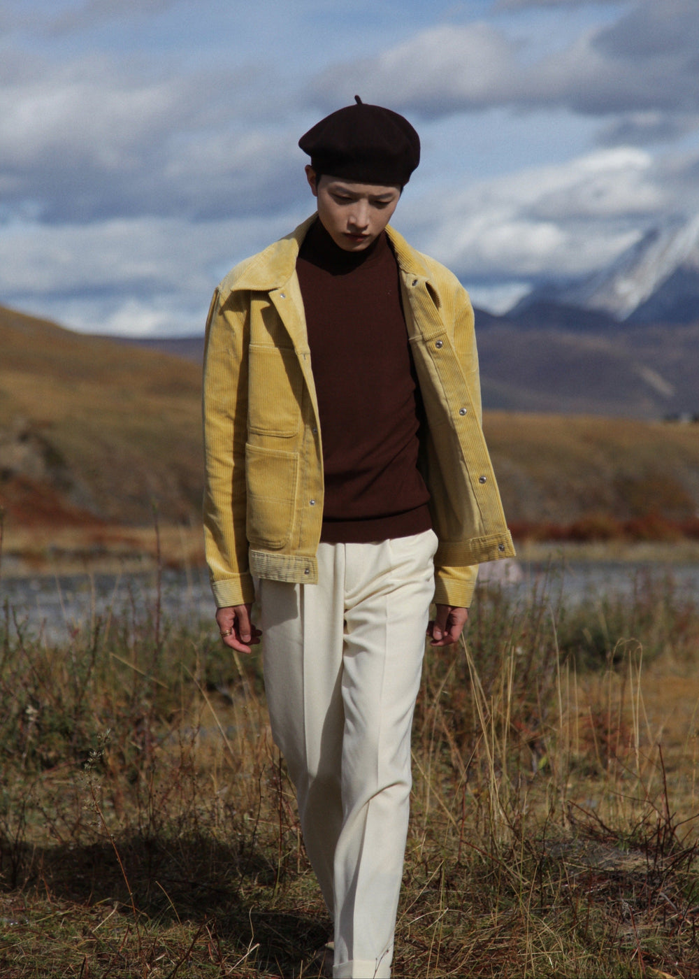  Model wearing Moonland creamy yellow corduroy workwear jacket, front view in nature landscape, shiny silver snap button, with large patch pocket