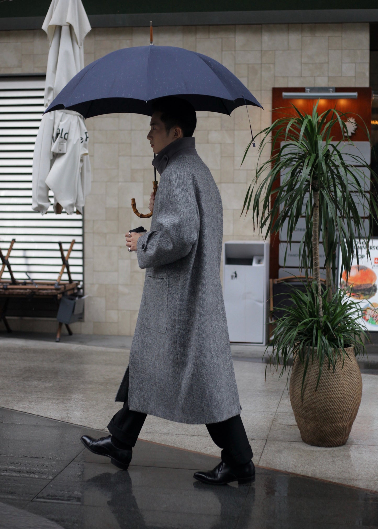 side view of Moonland's Balmacaan coat for men, made of Harris Tweed grey tone herringbone pattern. convertible collar, raglan sleeves with tab cuff, patch pocket, deep back vent, full length cut