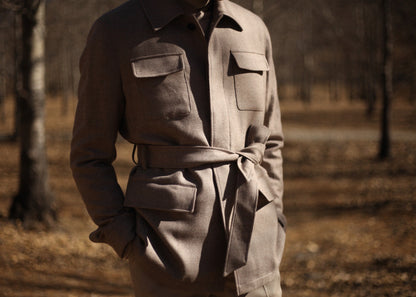 Model wearing Moonland's Altai safari jacket for men. showing the belt, chest pockets, and clean lines, front view. the clothes has a luster of the blend of cashmere, wool and cotton.