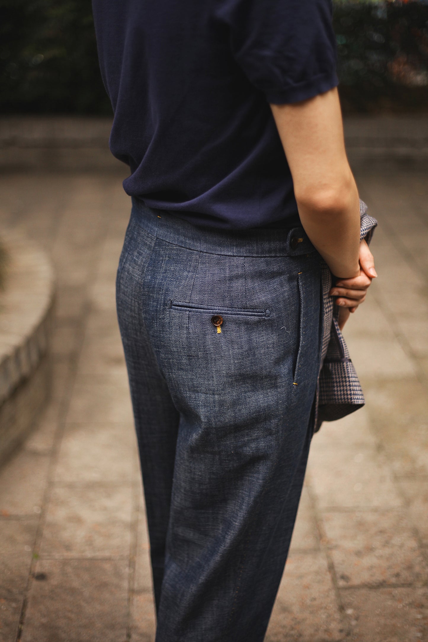 Model wearing Moonland Okayama Denim Trousers, back view showing welt back pockets with buttons and bright yellow buttonhole stitches.