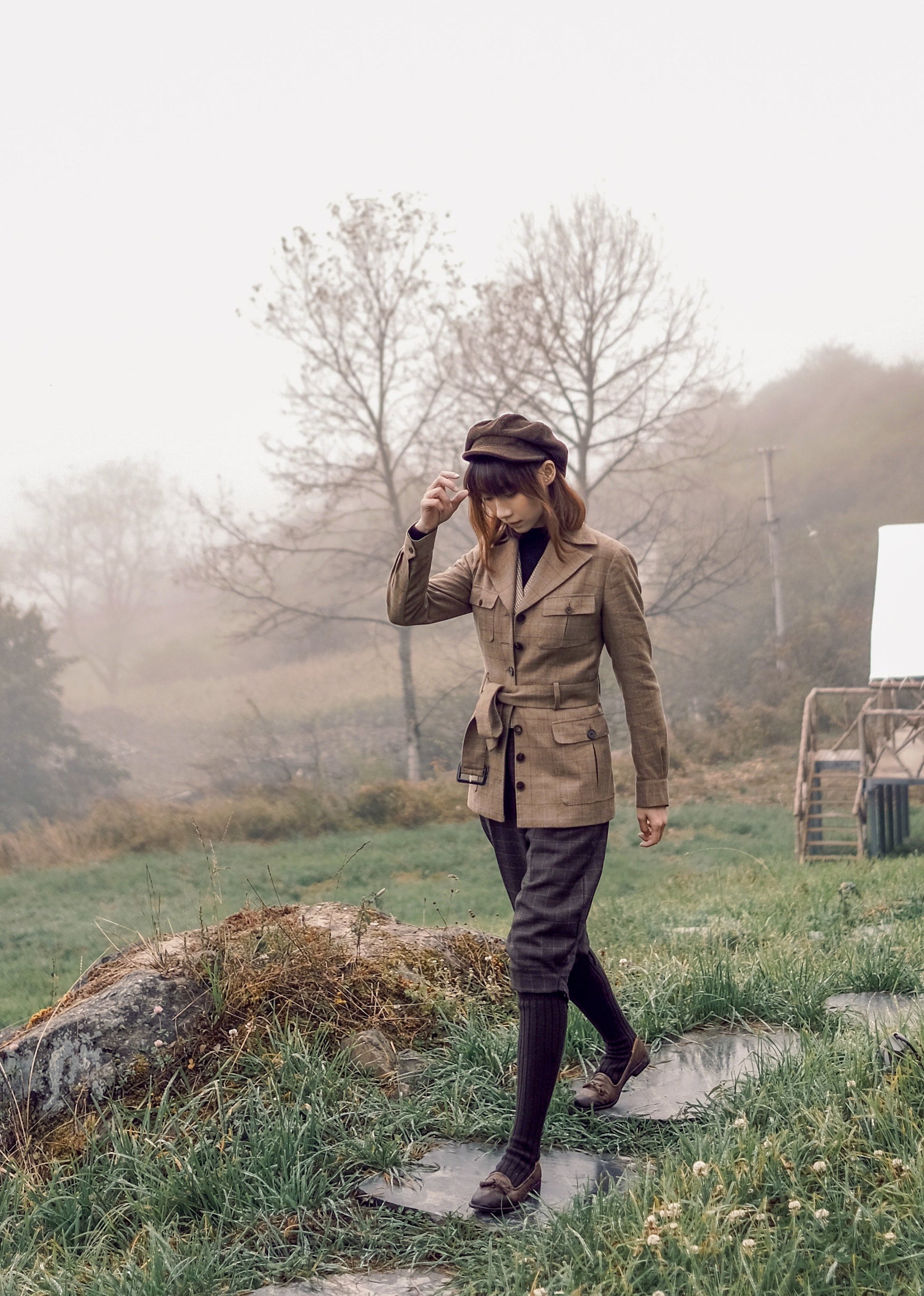 Moonland brown windowpane wool safari jacket side view, Ulster notch lapel, utility pockets with inverted pleats and defined waist with buckled belt.