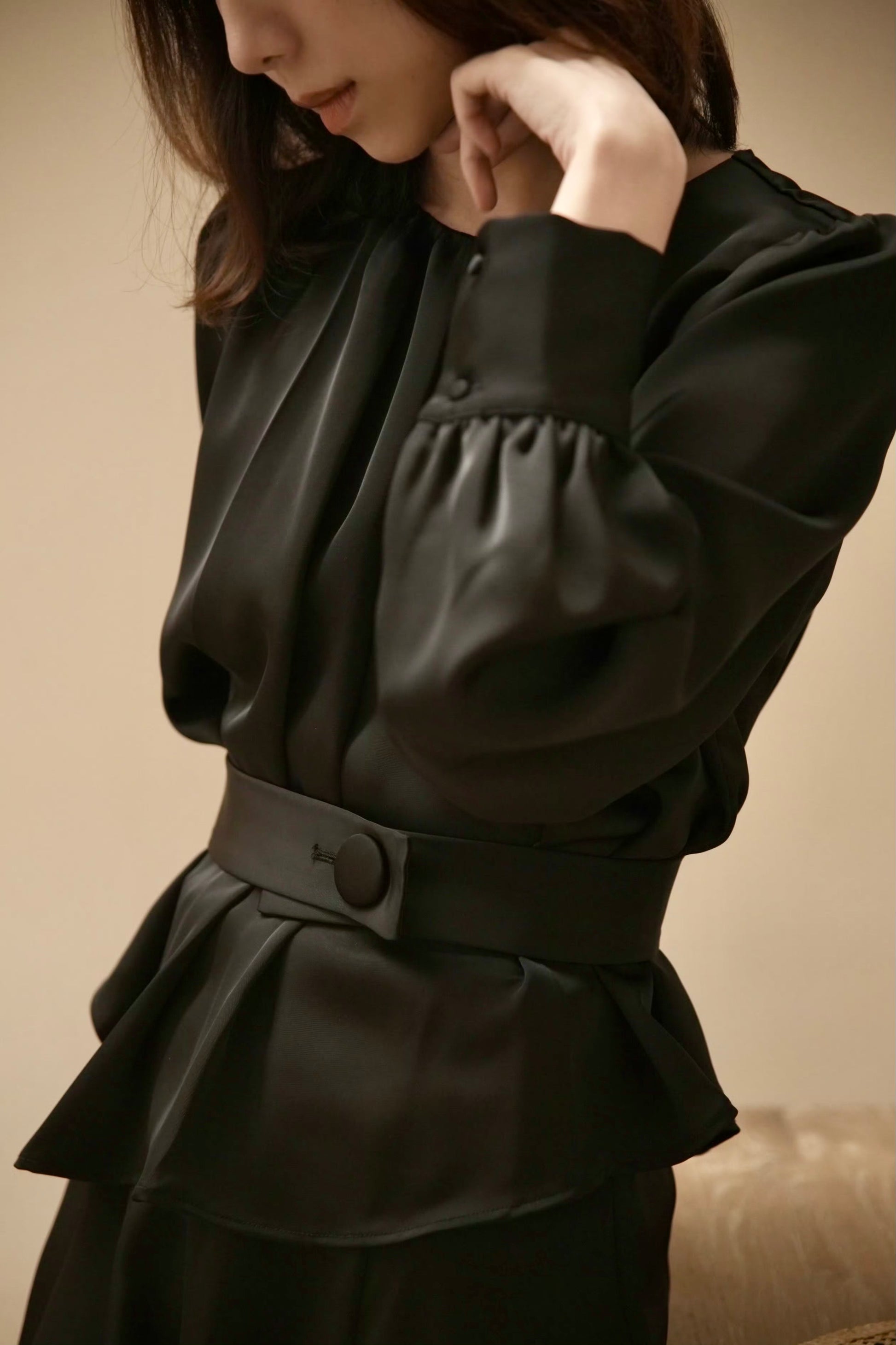 Moonland Silk Ripple Pleat Blouse, in black color, side front view with details, gathered round neckline, long puff sleeves with volume, cuff with covered round buttons, pleated peplum with self belt at the front and a large covered button, soft lustre 