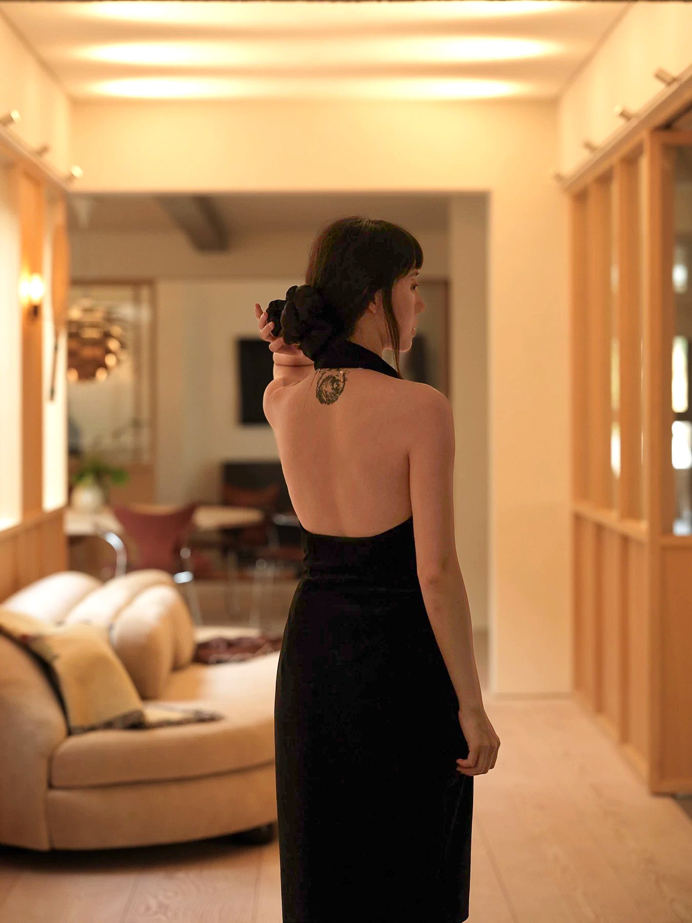 Moonland smoking velvet halter dress with suit front, indoor back view in warm light, in black silk velvet, sheath silhouette