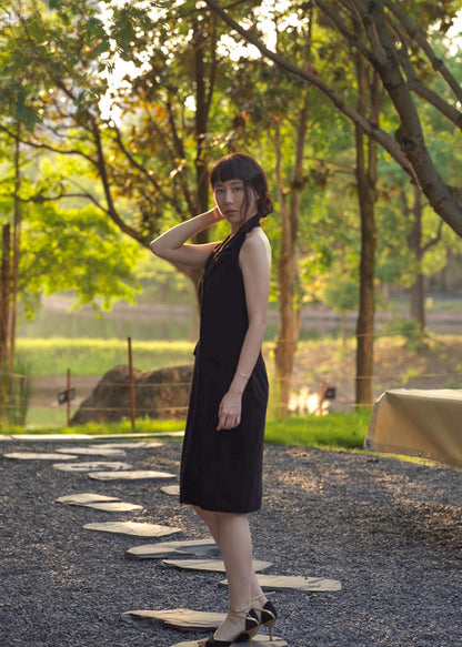 Moonland smoking velvet halter dress, side profile among trees, lapel detail and jetted flap pockets visible, in black silk velvet, sheath silhouette