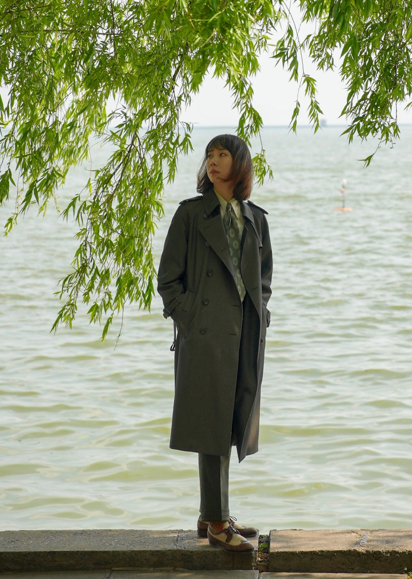 Moonland dark green trench coat with detachable down layer, double breasted with epaulettes and sleeve straps, front view under willow. #color_cypress-green