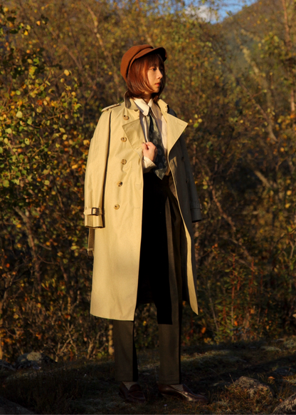 Person wearing a trench coat and hat standing in a forest with autumn foliage. #color_khaki