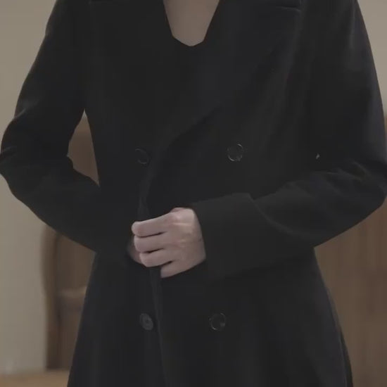 Video of Moonland modern redingote coat with cashmere. A women’s redingote coat shown in motion. The pleated back and deep vent create fluid stride and generous sweep. Peak lapels, double breasted front, and princess seams sculpt a long silhouette. Pure wool with smooth lining, full length. Ideal for evening and city promenades.