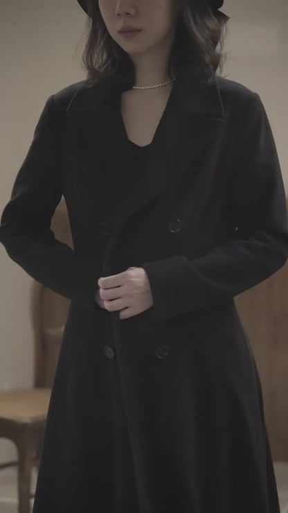 Video of Moonland modern redingote coat with cashmere. A women’s redingote coat shown in motion. The pleated back and deep vent create fluid stride and generous sweep. Peak lapels, double breasted front, and princess seams sculpt a long silhouette. Pure wool with smooth lining, full length. Ideal for evening and city promenades.